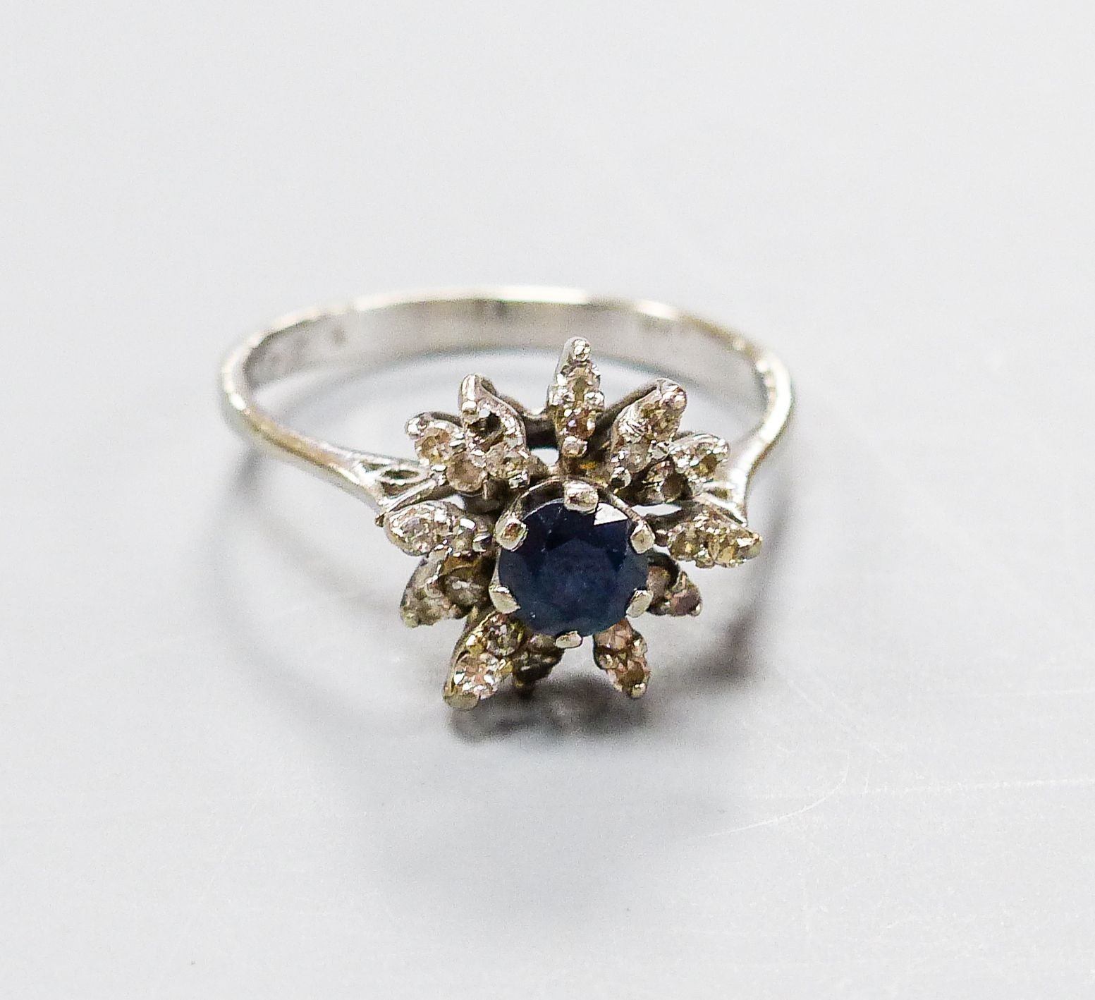 An 18ct white metal, sapphire and diamond set flower head cluster ring, size O, gross 3 grams.